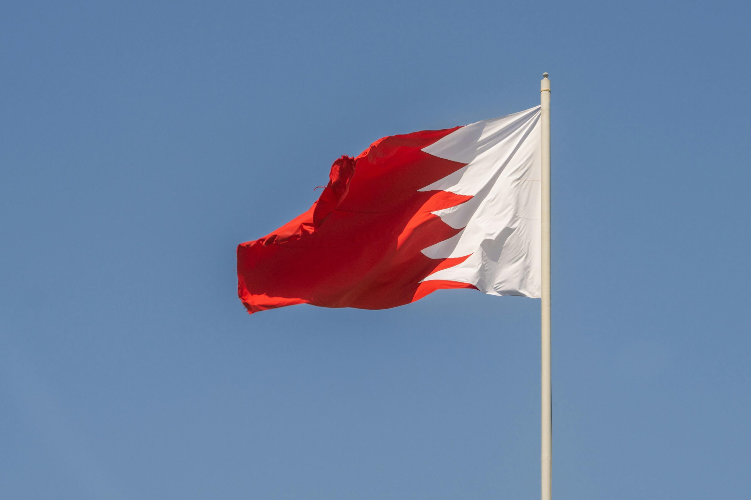 The Bahrain national flag capturing the vibrant red and white design against a clear blue sky.