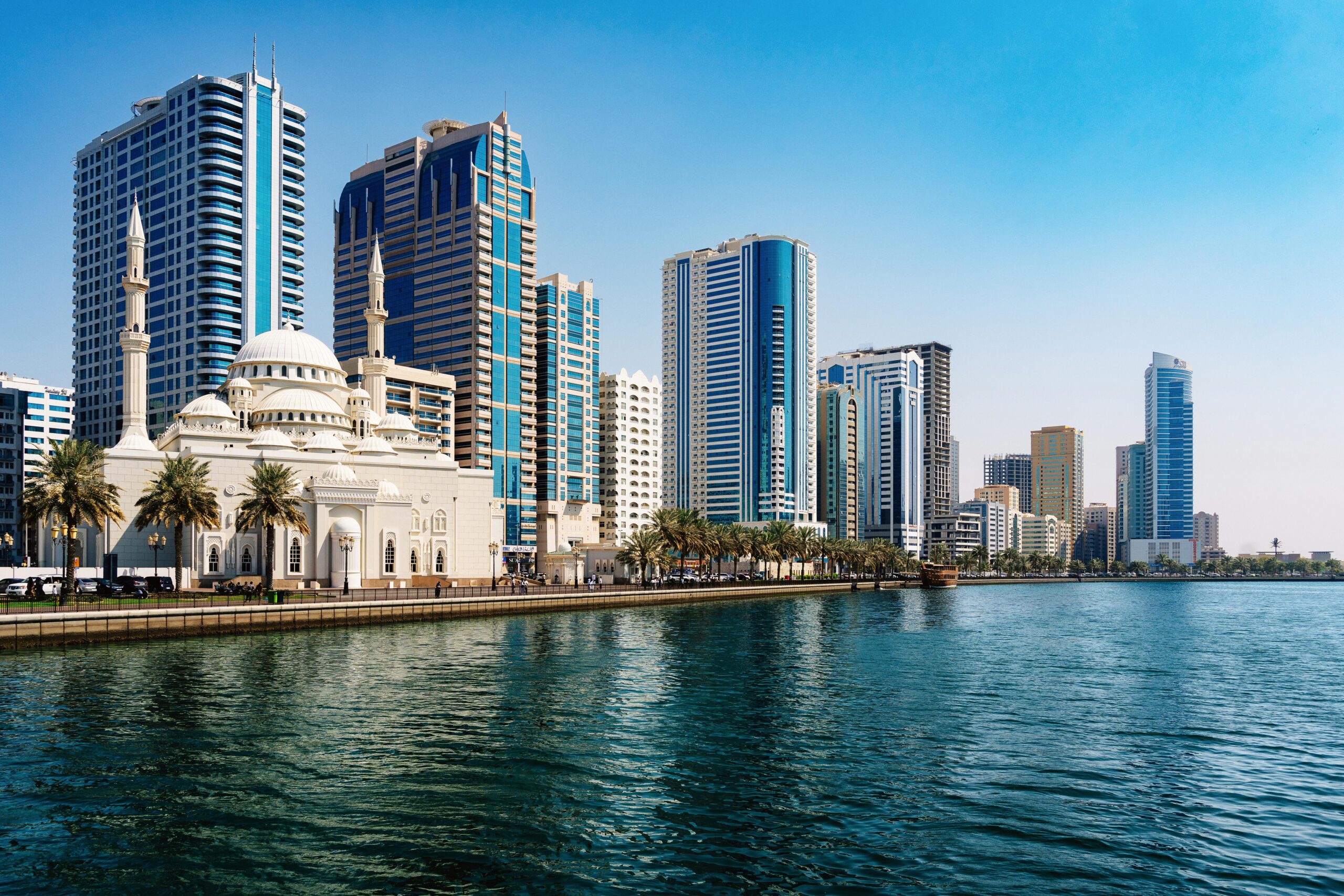 Captivating view of Sharjah's skyline with a prominent mosque by the waterfront under a clear blue sky.